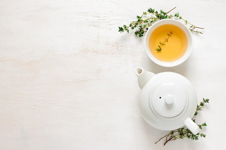 Fundo branco com xícara e bule de chá com ervas do lado