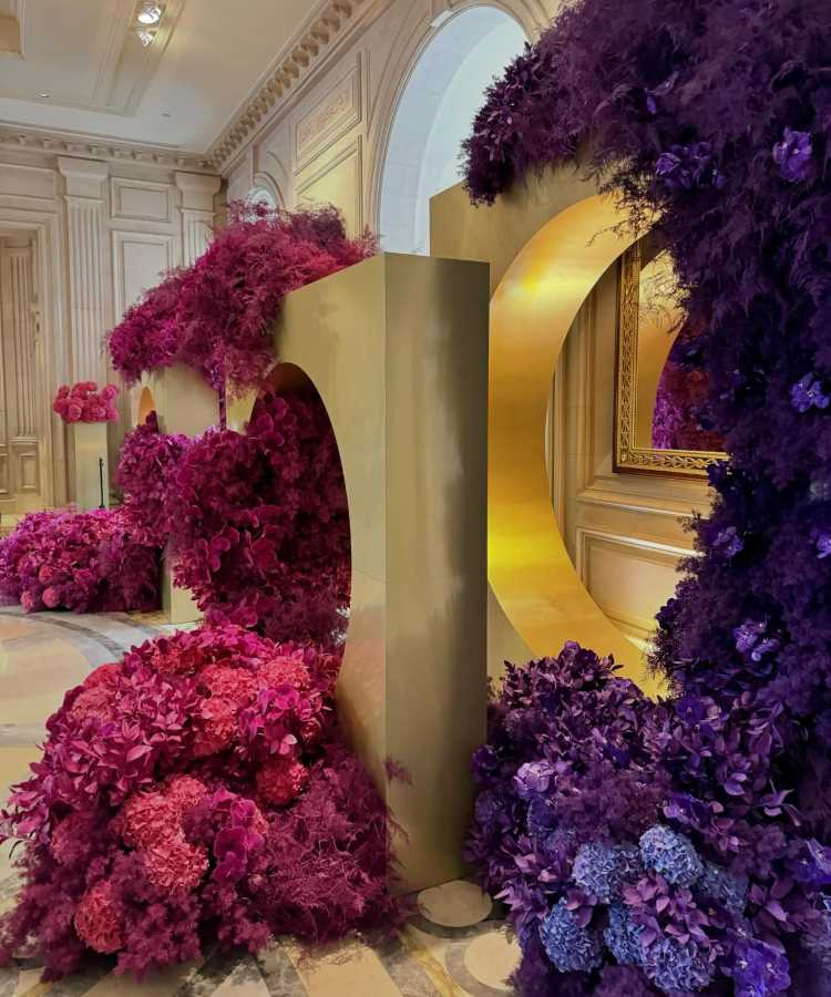 A imagem ilustra uma tendência de casamento que destaca o uso de estruturas metálicas douradas combinadas com arranjos florais exuberantes em tons de rosa e lilás. Esse design cria um ambiente sofisticado e moderno, ideal para casamentos que buscam um impacto visual marcante. As flores vibrantes contrastam elegantemente com o dourado, trazendo um toque de glamour e inovação. Essa abordagem enfatiza a importância de uma decoração ousada e luxuosa, perfeita para casais que desejam um evento memorável e cheio de personalidade.