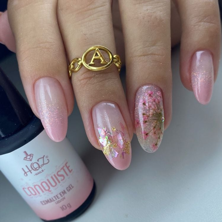 Foto de mão de pessoa de pele clara com unha almond em rosa claro com brilho e flores encapsulados