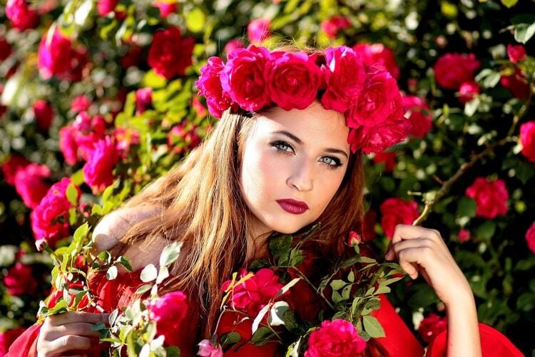 Mulher com batom vermelho e coroa de rosas vermelhas na natureza