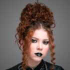 Fundo cinza com foto de mulher ruiva usando maquiagem roqueira para o Dia do Rock: smokey eyes e batom preto