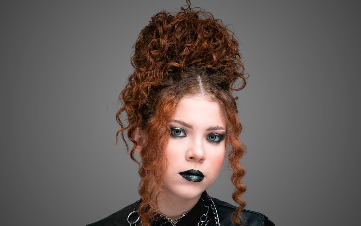 Fundo cinza com foto de mulher ruiva usando maquiagem roqueira para o Dia do Rock: smokey eyes e batom preto