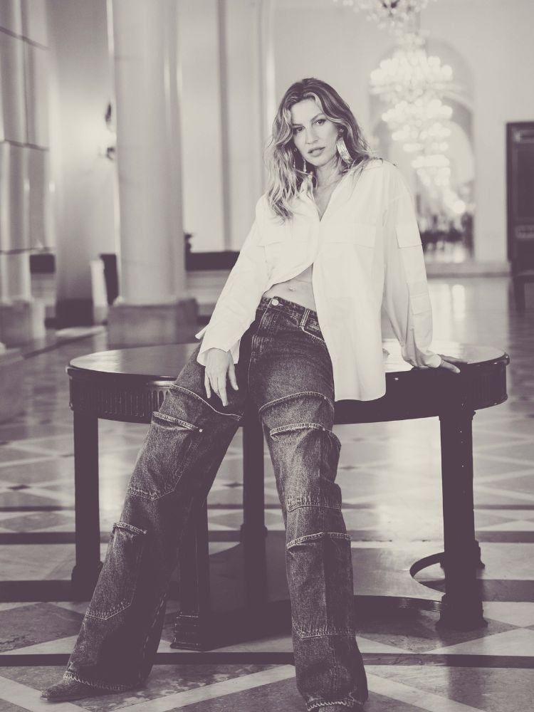 Foto em preto e branco da modelo Gisele Bündchen usando camisa branca oversized e calça jeans da Colcci