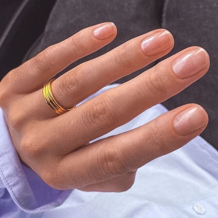 Foto de mão de mulher com unhas naturais, curtas e arredondadas. No dedo anelar, há uma aliança de ouro