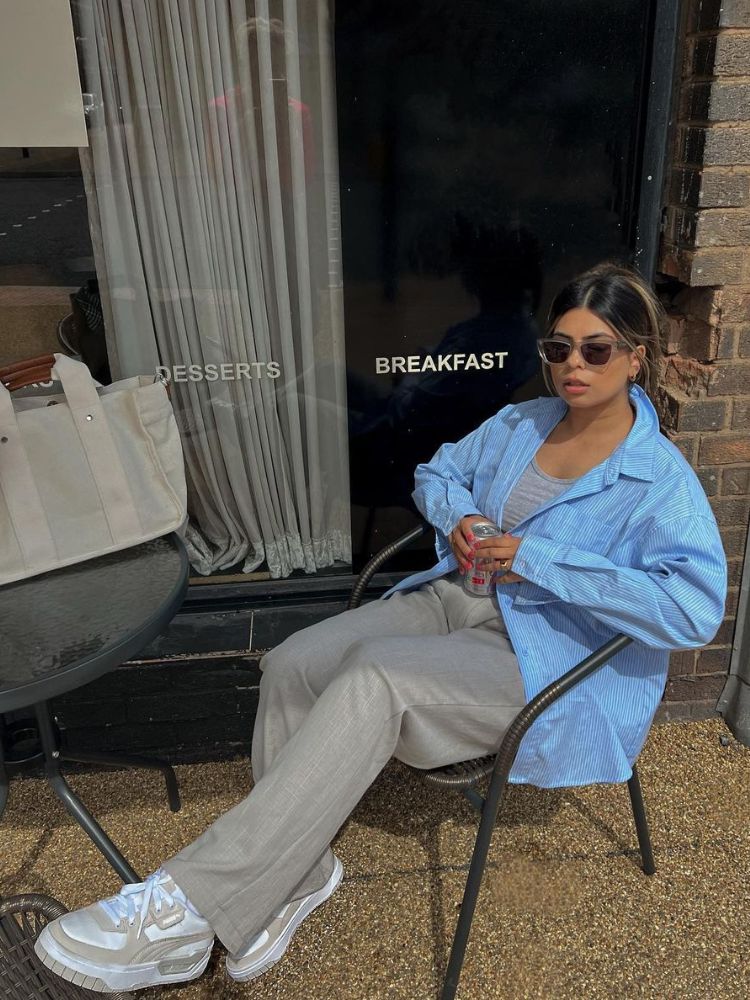 Mulher usando regata cinza, camisa oversized listrada azul e calça de alfaiataria cinza com tênis