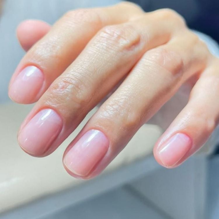 Foto de mão de mulher com unhas arredondadas e curtas na técnica de manicure japonesa