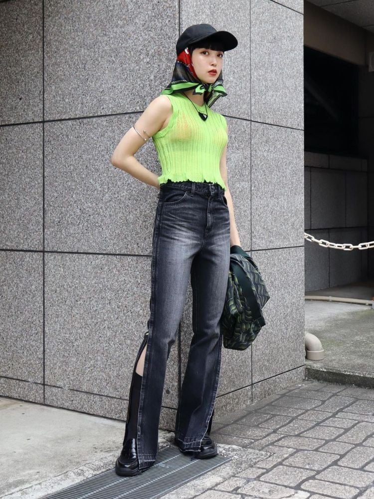 Mulher usando boné preto, lenço estampado, regata verde, calça jeans escura e mocassim preto