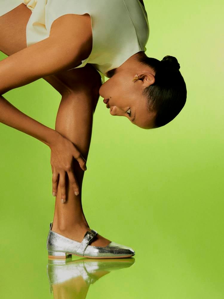 Uma modelo em uma pose atlética, usando sapatos metalizadoss, shorts e uma blusa verdes; o fundo também é verde.