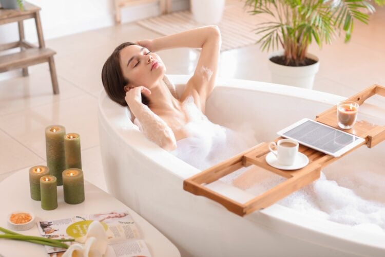 Foto de mulher de pele clara relaxando na banheira com velas, café, plantas, bebidas e produtos de beleza