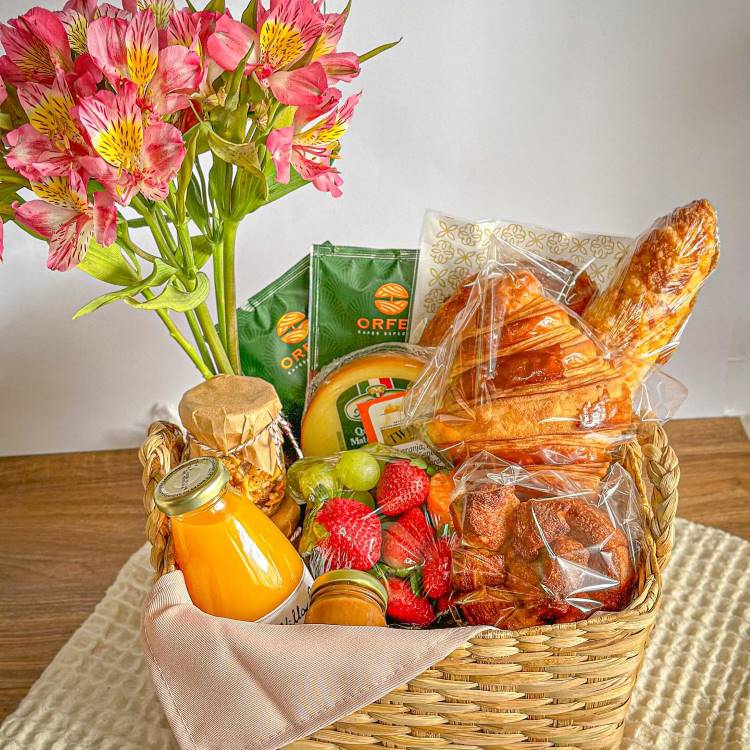 Cesta com suco de garrafa, frutas, pães, chá e flor