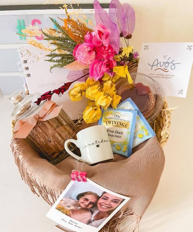 Cesta de Dia dos Avós com pote de vidro com doces, chás, torta de goiabada, caneca, livro de orações, flores, foto