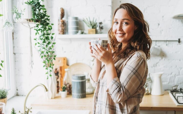 Foto de mulher usando camisa xadrez em sua cozinha e tomando chás para infecção urinária