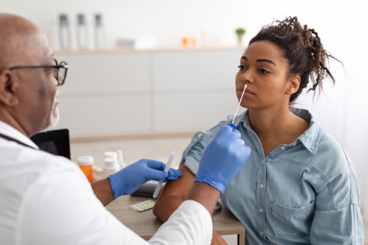 Mulher de pele negra usando camisa azul sentada de frente para médico de jaleco que está perto de realizar o exame pcr na mulher 