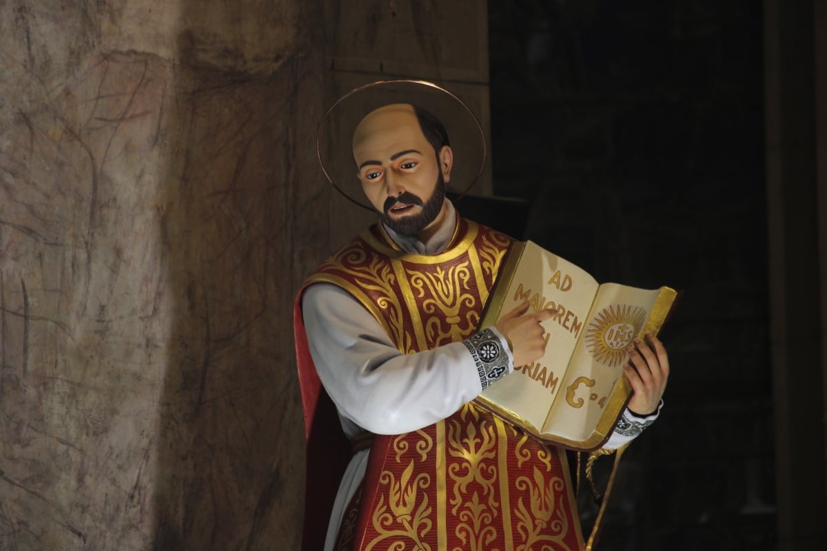 Foto de estátua de Santo Inácio de Loyola, com vestes vermelhas e douradas e segurando um livro aberto