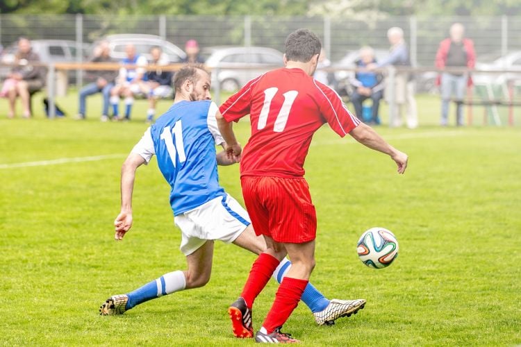 Duas pessoas jogando futebol, ambos camisa 11, um usando uniforme azul e branco e outro usando uniforme vermelho