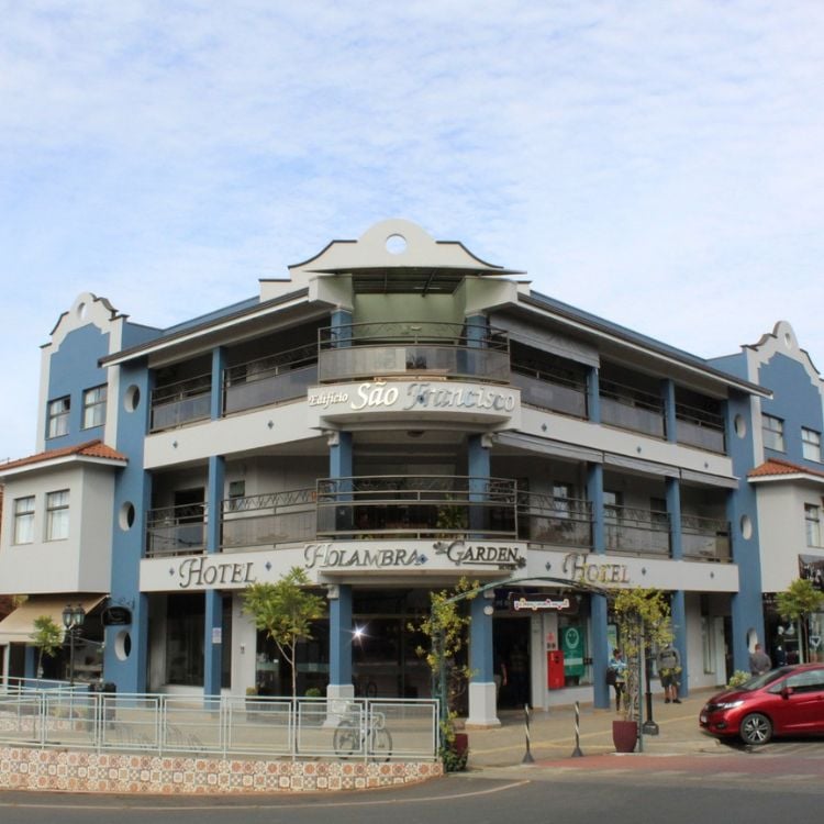 Fachada do Hotel Holambra Gaden, em bege com detalhes azuis, varandas e céu azul ao fundo