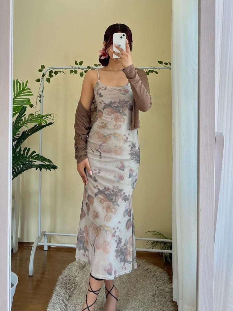 Mulher de pele clara tirando foto no espelho usando vestido midi cinza claro com desenhos pastéis e cardigan bege 