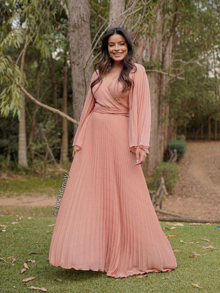 Mulher de pele morena usando vestido fluido bege com fundo rosado, de mangas longas