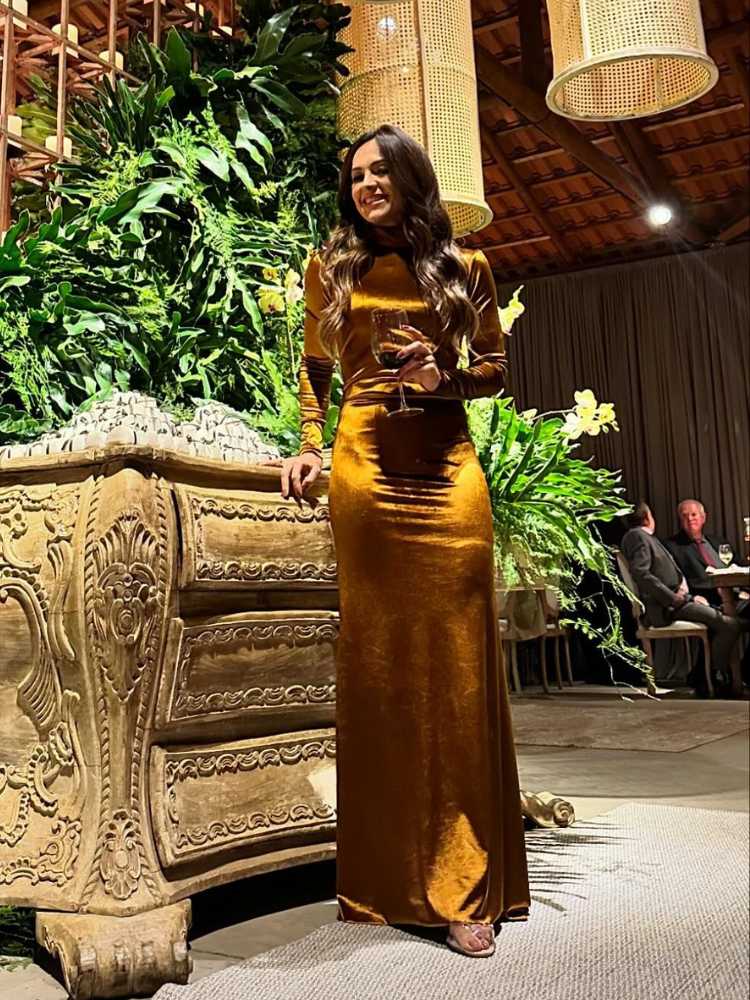 Mulher de pele clara usando vestido de veludo dourado longo e de mangas longas em casamento decorado com muitas plantas