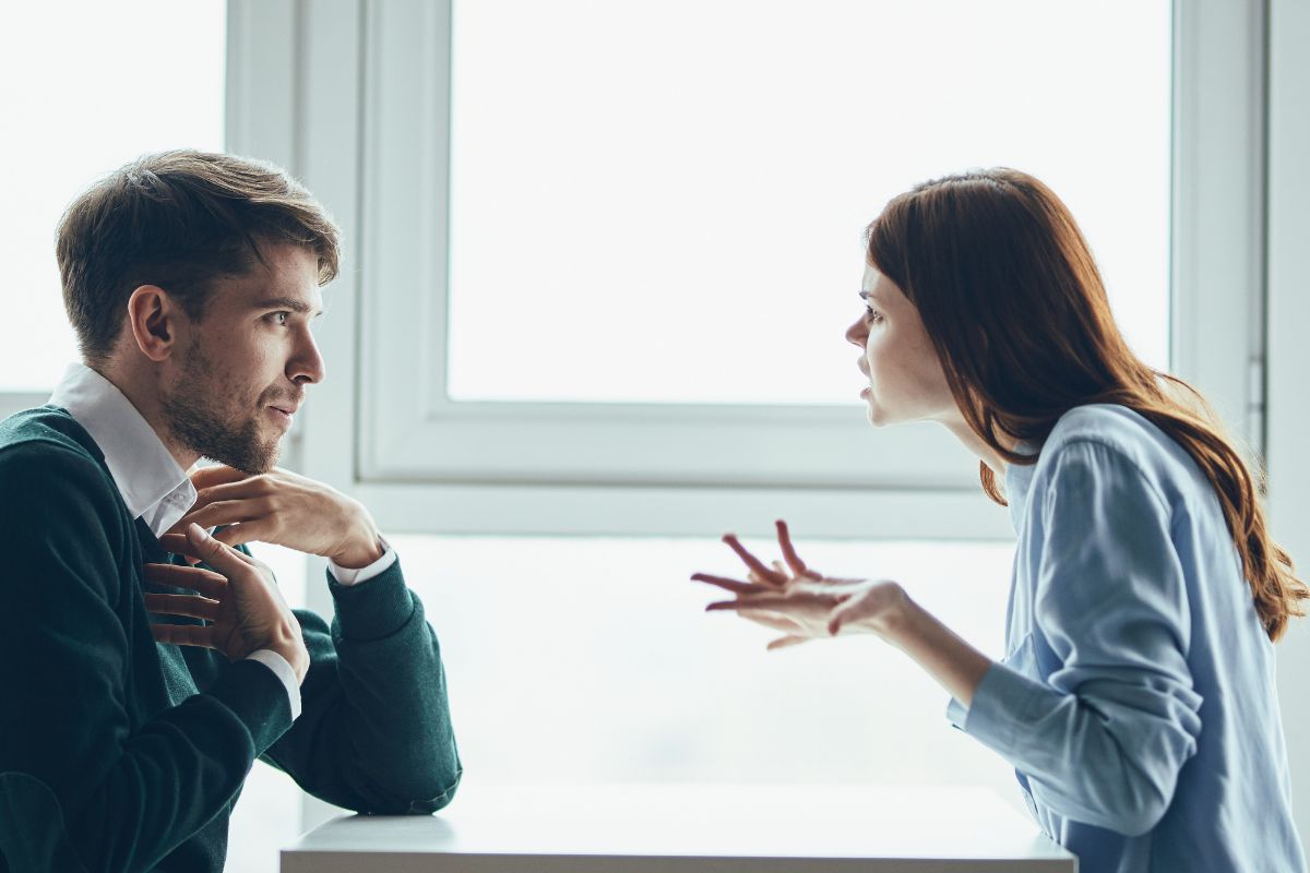 Mulher de pele clara usando blusa azul e homem de suéter verde discutindo