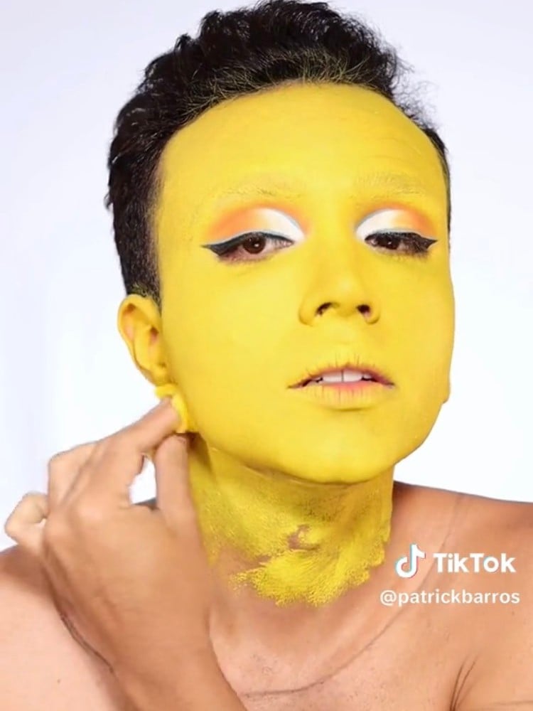 Homem de pele morena com sombra laranja e branca se pintando de amarelo