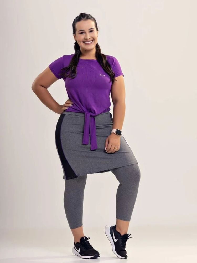 Mulher de pele clara usando blusa roxa e saia-calça cinza 