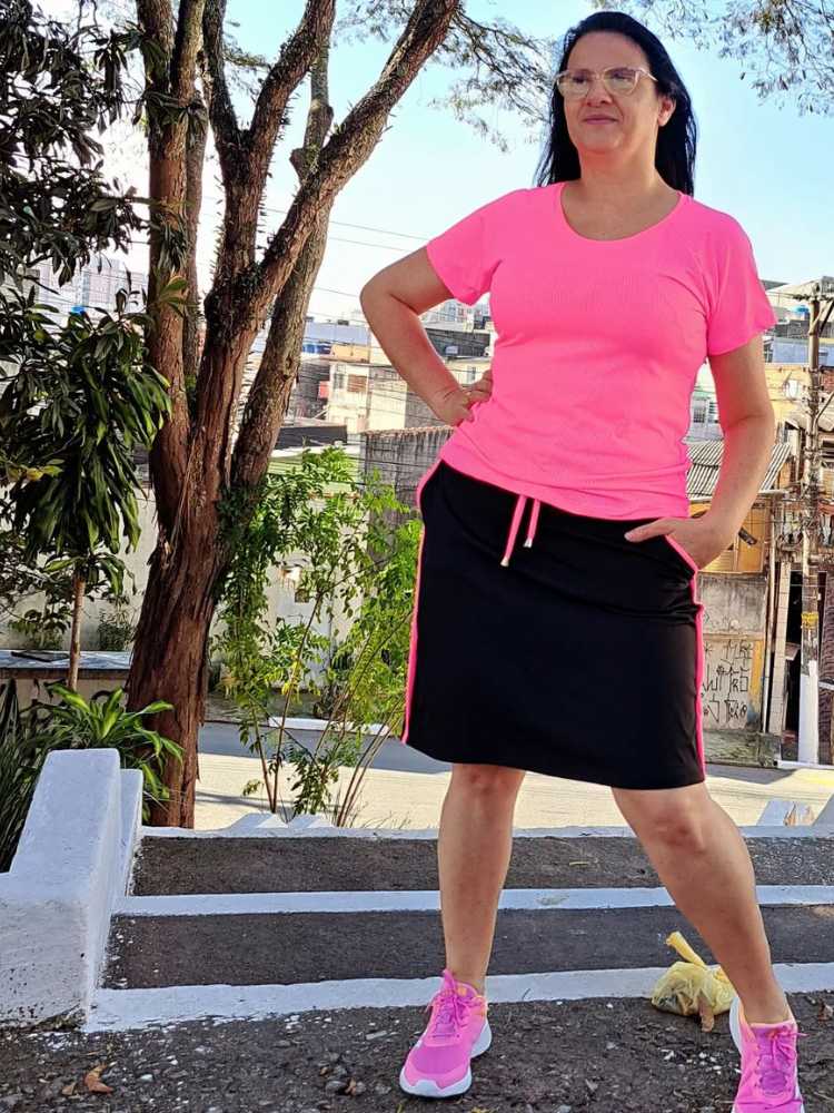 Mulher de pele clara usando blusa rosa e shorts saia preto