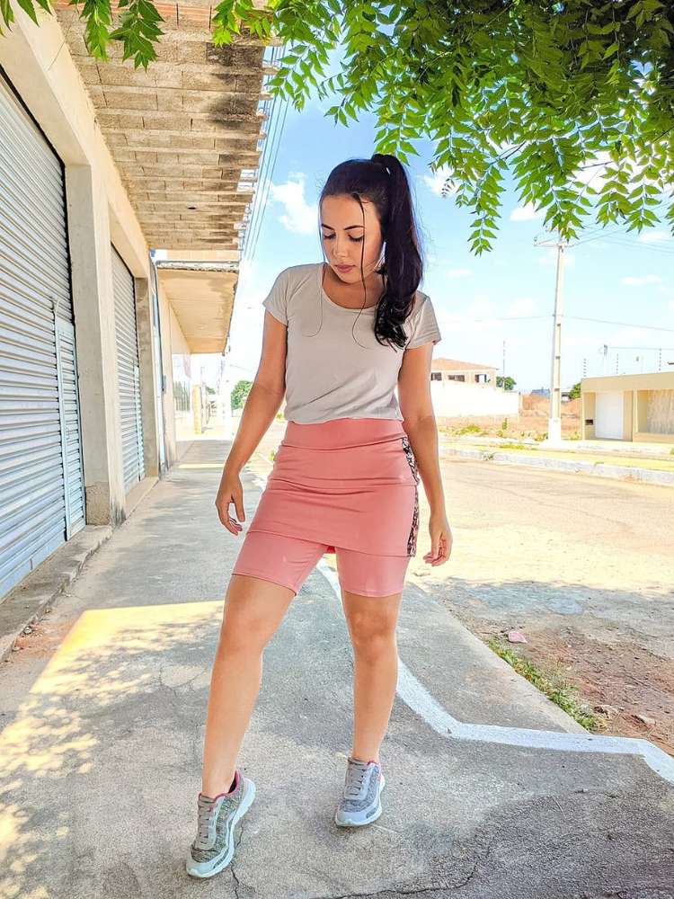 Mulher de pele clara na calçada usando blusa branca e shorts-saia rosa