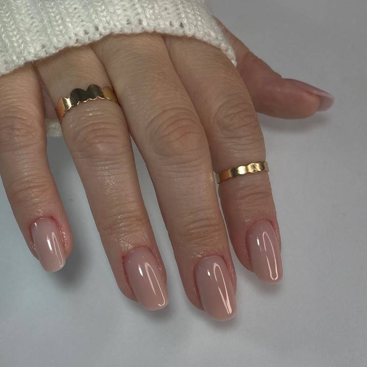 Esmaltação nude em unhas grandes arredondadas. A mão possui anéis