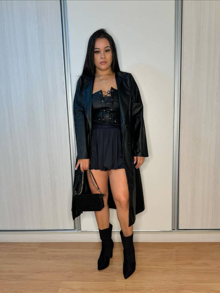 Mulher de pele clara usando corset preto, minissaia preta, bota cano médio e sobretudo preto