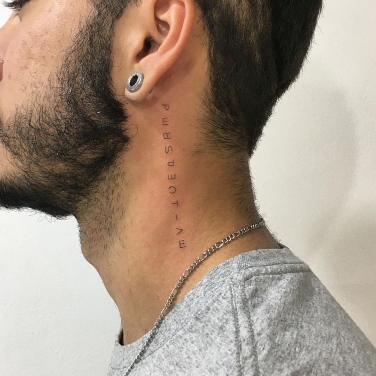 A imagem mostra uma pessoa de perfil com barba e cabelo curto. Ela tem uma tatuagem no pescoço com a palavra "PERSPECTIVE" escrita verticalmente em letras finas. A pessoa usa um alargador na orelha e uma corrente prateada.