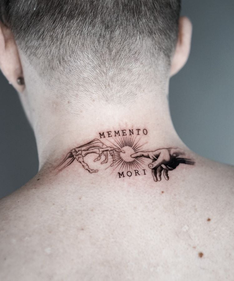 A imagem mostra uma pessoa de costas com cabelo curto. Ela tem uma tatuagem no pescoço que representa duas mãos se tocando, uma esqueleto e outra humana, com as palavras "Memento Mori" acima e abaixo. A tatuagem é detalhada em preto e ocupa a parte superior das costas.