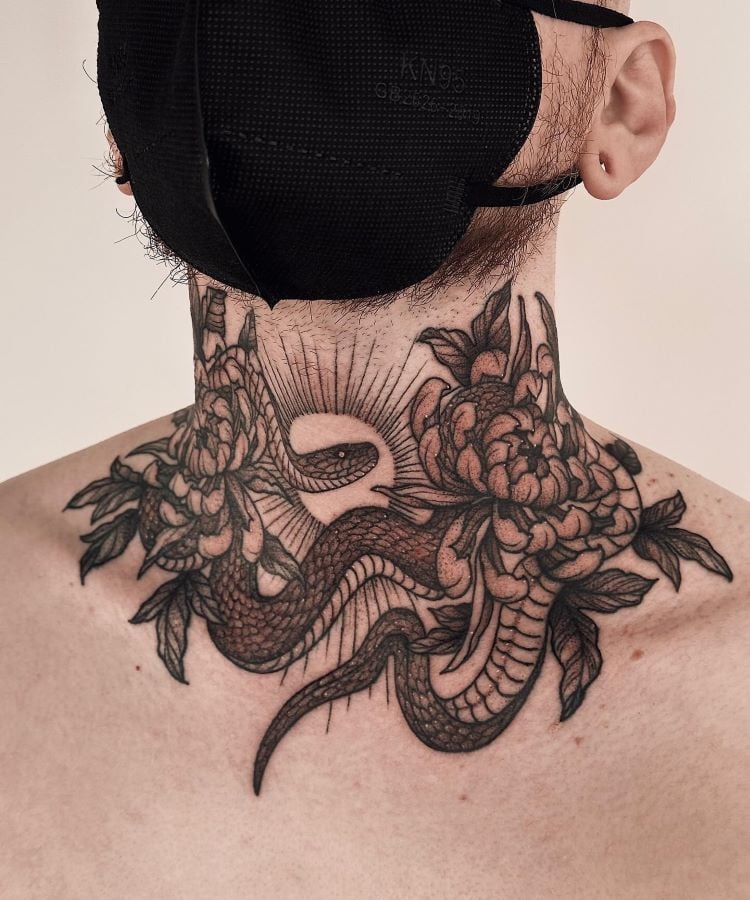 A imagem mostra uma pessoa usando uma máscara preta. Ela tem uma tatuagem no pescoço de uma cobra entre flores, com detalhes finos em preto. A tatuagem cobre a parte da frente do pescoço e se estende até a parte superior das costas.