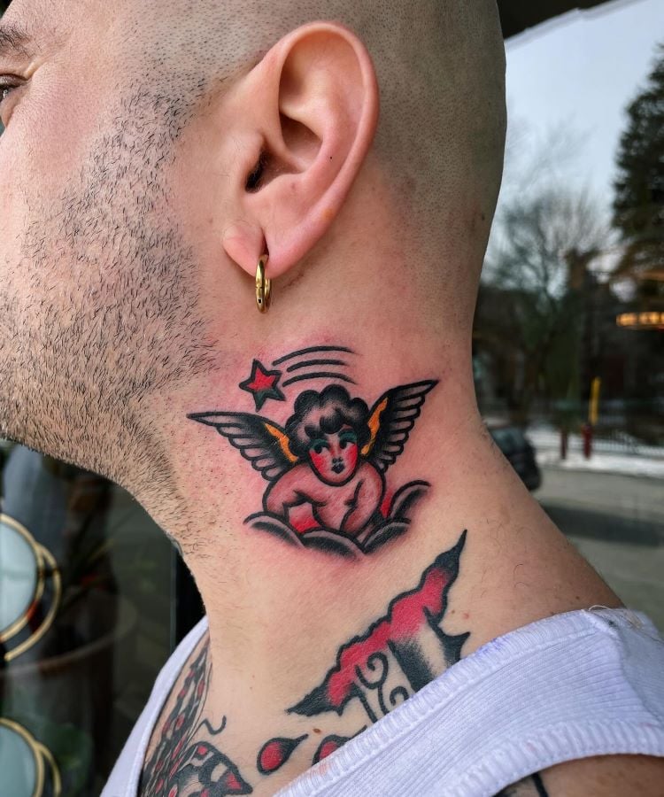 A imagem mostra uma pessoa de perfil com uma tatuagem no pescoço representando um anjo com asas e uma estrela vermelha acima. A pessoa tem a cabeça raspada e usa um brinco dourado de argola na orelha esquerda.