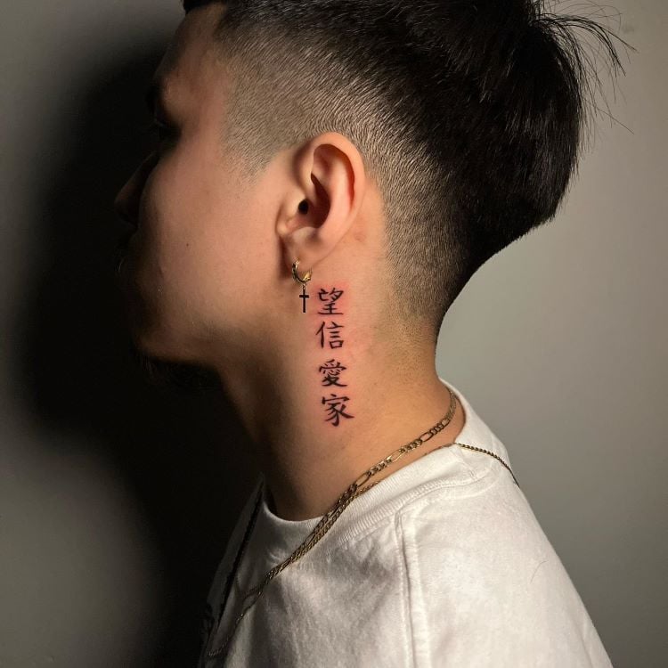 A imagem mostra uma pessoa de perfil com cabelo curto. Ela tem uma tatuagem no pescoço de caracteres chineses verticais em preto, significando "esperança", "fé", "amor" e "família". A tatuagem está localizada na lateral do pescoço, perto da orelha, onde a pessoa usa um brinco de cruz.