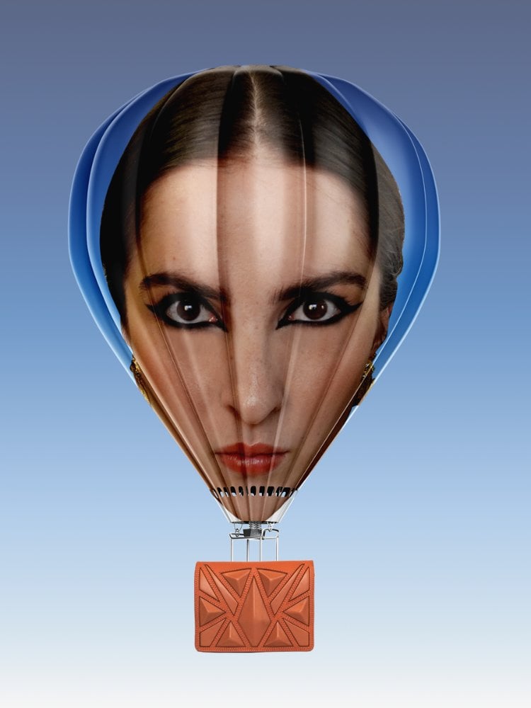 Balão com rosto de Luiza  Mallmann, diretora criativa da Ryzí, uma mulher de pele clara e cabelo escuro, com uma bolsa marrom abaixo, em um fundo azul