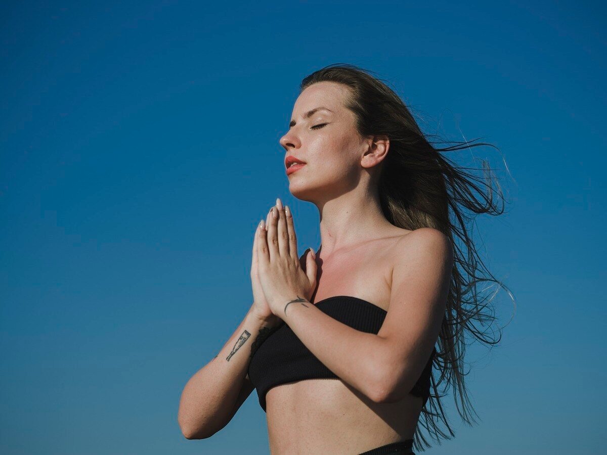 Mulher com as mãos no peito em forma de prece meditando em um fundo azul