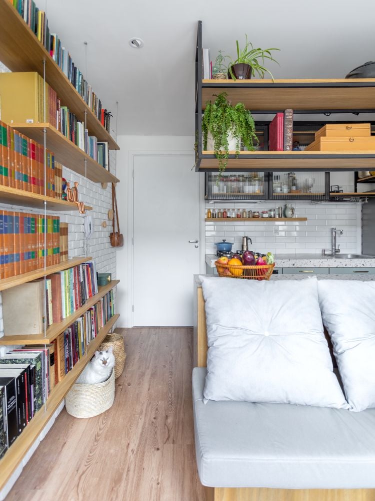 Sala integrada de apartamento de 25m² decorado com parede de azulejo branco e estante de livros