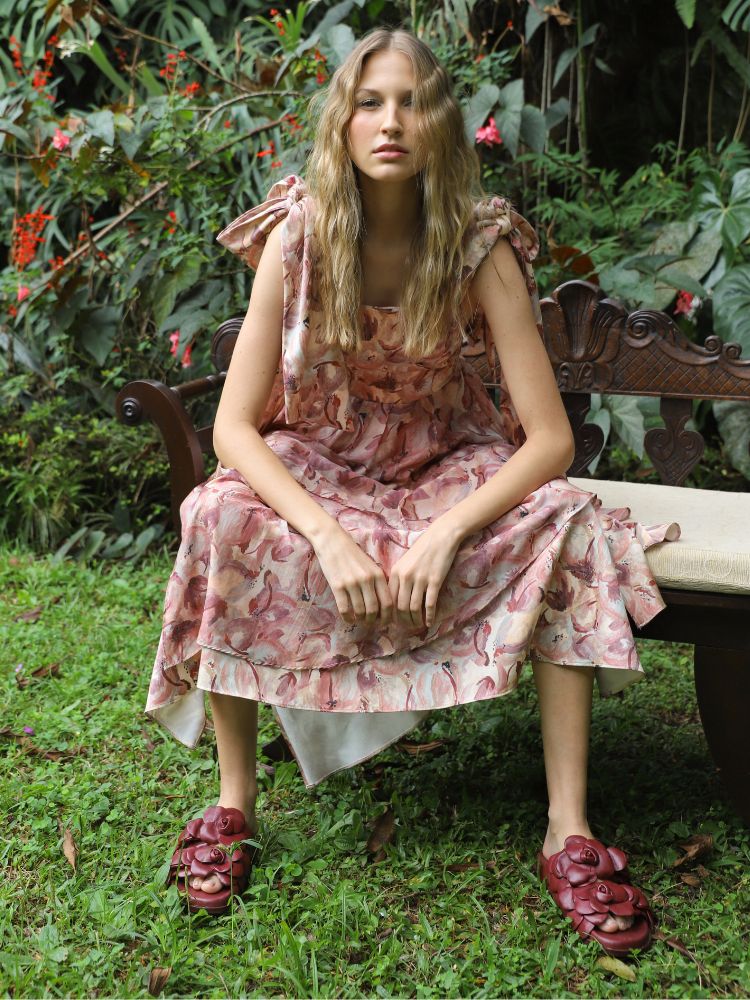 Foto de mulher usando vestido mídi com estampa floral rosa sentada em um banco de madeira em um jardim