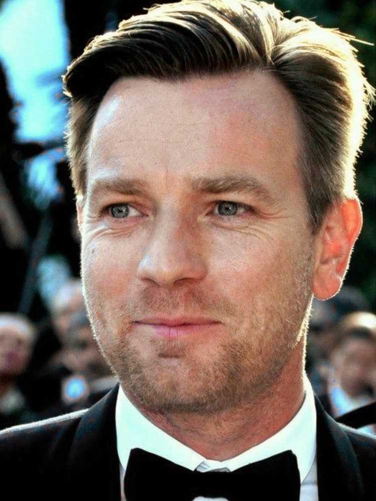 A imagem mostra um homem (Ewan McGregor) de cabelo castanho claro, penteado para trás. Ele tem olhos claros e está sorrindo levemente. Ele veste um smoking preto com uma camisa branca e uma gravata borboleta preta. O fundo está desfocado, sugerindo que ele está em um evento formal.