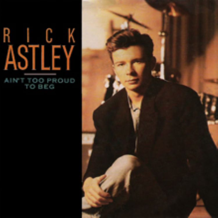 Rick Astley, um dos famosos dos anos 80, aparece na capa de seu single "Ain't Too Proud to Beg". Ele está sentado, vestindo um blazer escuro e calças claras, com um fundo que sugere um estúdio musical. A imagem captura seu estilo clássico e presença marcante na música pop.