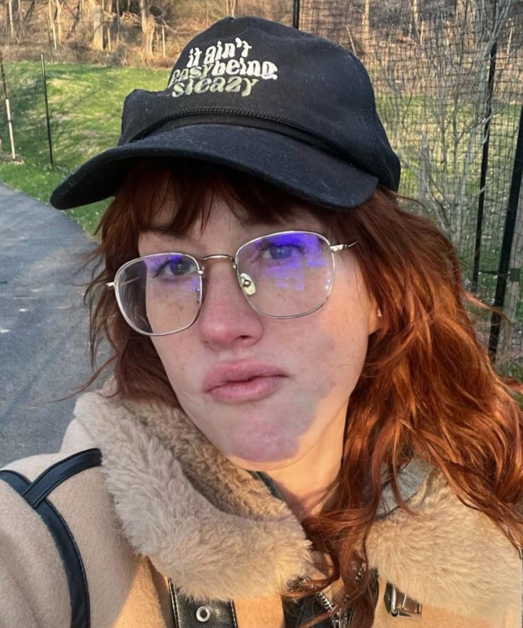 Molly Ringwald, uma das famosas dos anos 80, em uma foto recente. Ela está ao ar livre, usando óculos grandes, boné preto e casaco de inverno. Com expressão descontraída e sem maquiagem, a imagem mostra sua aparência atual e natural, contrastando com sua juventude nos anos 80.