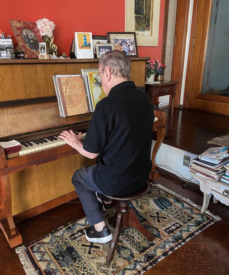 Caçulinha tocando piano em casa. O piano é decorado com fotos e cadernos