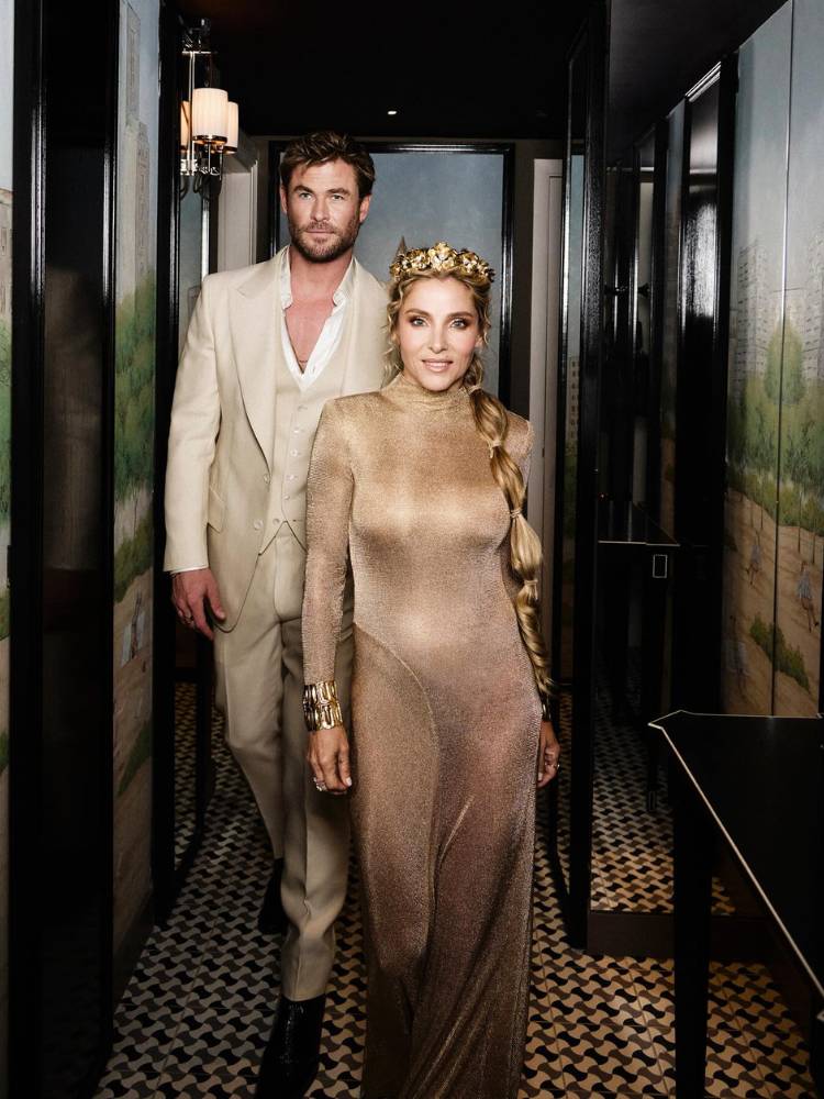 Chris Hemsworth e Elsa Pataky em ensaio fotográfico. Ele usa terno bege e ela usa vestido bege de veludo e uma coroa 