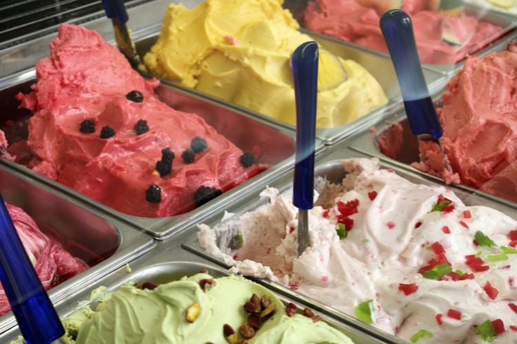 Foto de vitrine de gelato com opções de frutas vermelhas, pistache, massa amarela e bege 