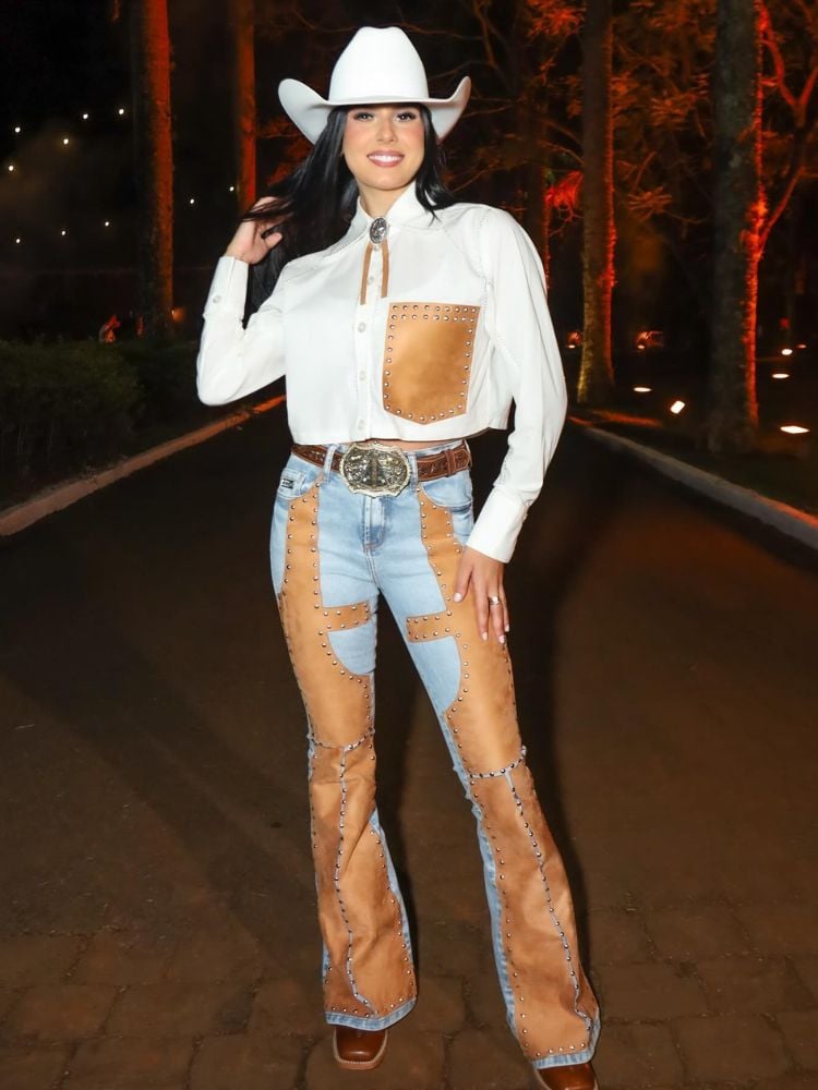 Ana Castela usando camisa branca com bolso de couro bege e calça jeans com mescla de couro bege, além de chapéu branco 