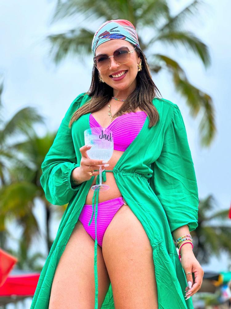 Mulher de pele clara usando biquíni roxo, saída de praia verde e lenço de seda azul e vermelho no cabelo 