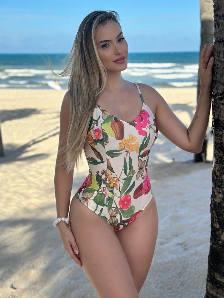 Mulher de pele clara na praia usando maiô estampado com flores, tudo em tons claros