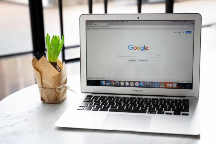 Um laptop MacBook Air aberto em uma mesa, exibindo a página inicial do Google. Ao lado, há uma pequena planta em um vaso de papel. Esta imagem representa o acesso ao Google Notebook LM, destacando a simplicidade e acessibilidade da plataforma.