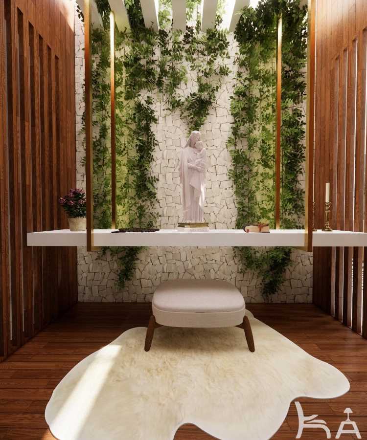 A imagem mostra um oratório em casa com um design moderno e elegante. No centro, há uma estátua branca de uma figura religiosa sobre uma mesa suspensa por hastes douradas. A parede de fundo é revestida com pedras brancas e decorada com plantas verdes que sobem verticalmente, criando um ambiente sereno. À esquerda da mesa, há um vaso com flores roxas, e à direita, uma vela em um castiçal dourado. No chão, um tapete claro está posicionado em frente a um banco acolchoado, sobre um piso de madeira. As paredes laterais têm painéis de madeira, adicionando um toque acolhedor ao espaço.